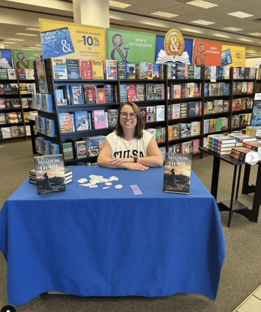 A woman sitting at a table in front of books.